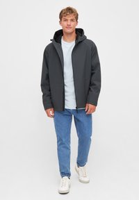 Donkergrijze hoodie met rits, gemaakt van gladde stof, gecombineerd met een lichtblauw t-shirt, blauwe jeans en witte sneakers.