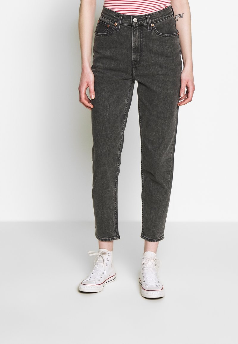 Vaqueros de mezclilla negros de cintura alta con pierna cónica, cierre de botón y diseño de cinco bolsillos. Llevados con zapatillas de lona blancas.