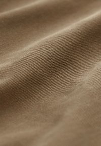 Gros plan sur un tissu doux brun avec une texture côtelée diagonale et des plis doux créant des ombres et des reflets.