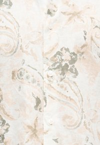 Κοντινό πλάνο λευκού υφασμάτινου πουκαμίσου με μπεζ και γκρι σχέδιο πεϊσλί και τρία λευκά κουμπιά στο κέντρο.