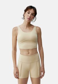 Beige sportsbh og matchende højtaljede shorts, lavet af strækbart materiale med en glat overflade og minimale sømme.