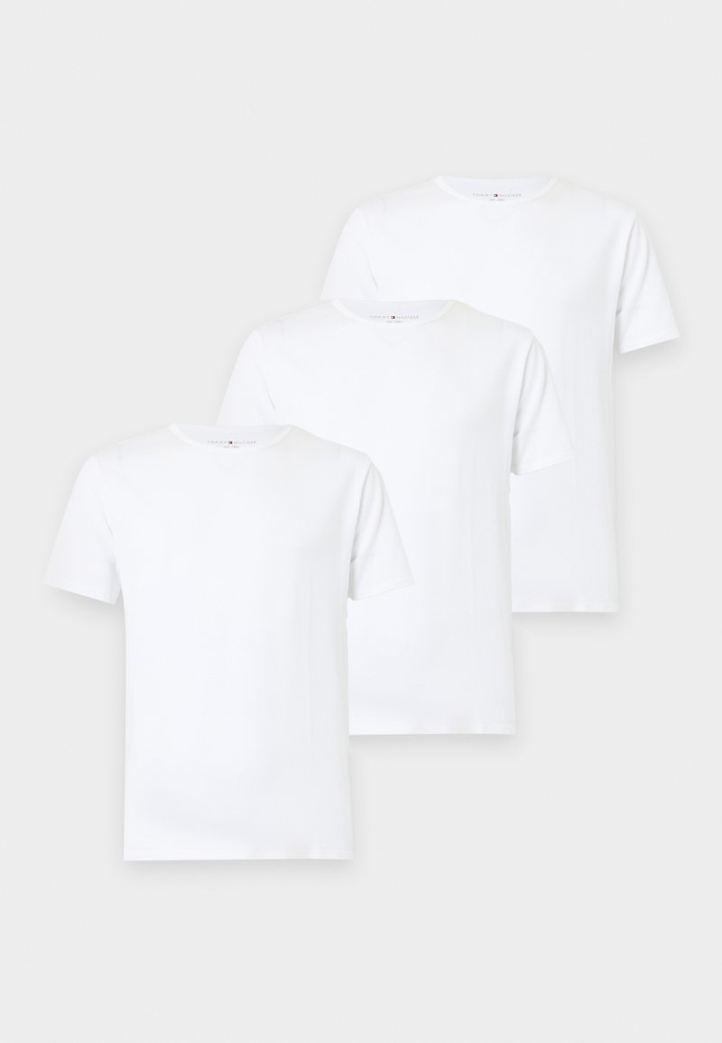 Trois t-shirts blancs unis à manches courtes et col rond, disposés en chevauchement décalé sur un fond clair.