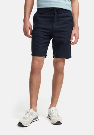 Marineblå shorts lavet af en bomuldsblanding med elastisk talje og dekorativ snor. Sammen med grå og hvide træningssko.