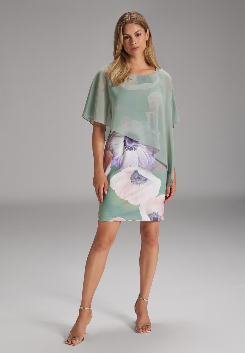 Abito floreale con sovrapposizione verde menta, caratterizzato da grandi fiori pastello. L'abito è aderente, con una texture liscia e maniche corte.