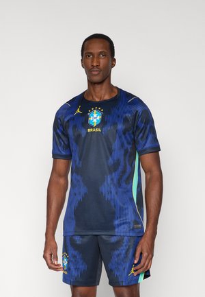 Tmavomodrý futbalový dres s grafickou textúrou, ozdobený zelenými akcentmi a logom národného tímu Brazílie. Dopĺňa ho zodpovedajúci pár šortiek.