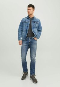 Chaqueta de mezclilla en azul claro con bolsillos clásicos, combinada con una camiseta gris y jeans ajustados azul, complementada con zapatillas grises.