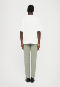 White short-sleeve t-shirt and light green tailored trousers, displayed from the back. Trousers are textured with a subtle pattern.