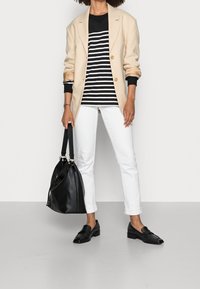 Beige Blazer mit goldenen Knöpfen, schwarz-weiß gestreiftem Hemd, weißen Jeans, schwarzen Slippern und einer schwarzen Ledertasche. Einfaches, modernes Design.