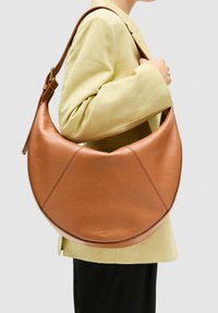 Brun læder hobo taske med en glat tekstur, afrundet form og accentuerede syninger. Har en enkelt skulderrem og en subtil logo detalje.