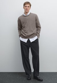 Brauner Strickpullover über einem weißen Kragenhemd und schwarzen Hosen getragen; verfügt über eine lockere Passform und eine glatte Textur; getragen mit schwarzen Loafers.