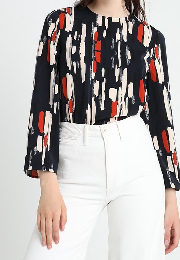 Långärmad blus i marinblått med abstrakt penseldragmönster i röd, krämfärgad och svart. Slätt tyg med rund halsringning. Vita högmidjade byxor.