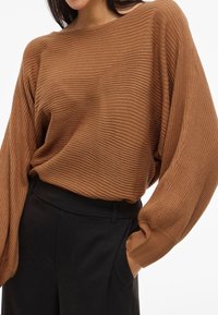 Brown ribbed knit sweater with a wide neckline and oversized sleeves, paired with tailored black trousers featuring side pockets.