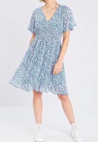 Niebieska sukienka w kwiaty z krótkimi rękawami, dekoltem w serek, marszczonym korpusem i falbaniastym dołem. Posiada biały wzór kwiatowy, noszona z białymi trampkami.