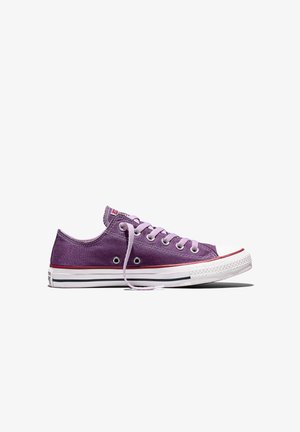 Baskets basses en toile violette avec une semelle en caoutchouc blanche, un embout blanc, des lacets roses et des détails à rayures rouges et noires, présentées de profil.