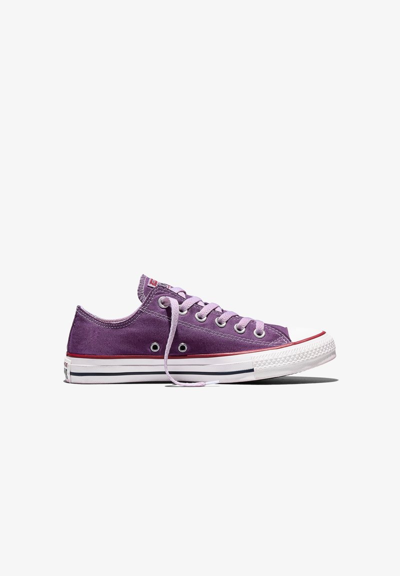 Lila Canvas-Turnschuh mit niedrigem Schnitt, weißer Gummisohle, weißer Zehenkappe, pinkfarbenen Schnürsenkeln und roten sowie schwarzen Streifendetails, seitlich gezeigt.