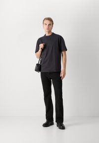 Camiseta negra de manga corta en un corte relajado, combinada con jeans negros de pierna recta y botines negros. Se lleva un pequeño bolso cruzado negro.