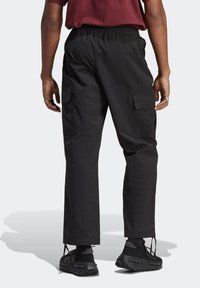 Černé nákladní kalhoty s elastickým pasem, bočními kapsami a volným střihem. Nošeny s černými teniskami s texturovanými detaily.