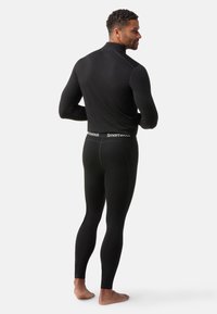 Top nero a maniche lunghe e leggings aderenti in materiale elastico. Presenta un colletto alto e un logo sulla vita. Tessuto morbido.
