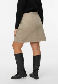 Beige A-formet nederdel lavet af struktureret stof, med en mellemlang længde; parret med høje sorte læderstøvler. Enkel og ren design.