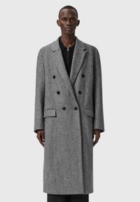 Divkrūšains pelēks zvīņotais mētelis ar iegrieztām atlociņām, priekšējām kabatām un melnajām pogām. Vilnas maisījuma audums ar gludu tekstūru.