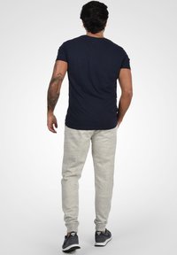 Navyblaues T-Shirt kombiniert mit hellgrauen Jogginghosen. Die Hosen haben eine weiche Textur mit Bündchen an den Knöcheln. Schwarze und graue Sneaker runden den Look ab.