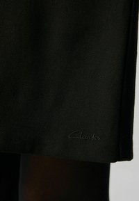Svart textilmaterial med en fiskbensstruktur och en broderad logotypdetalj, som visar en ren och modern design.