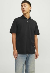 Čierna polo košeľa vyrobená z jemnej bavlny, s golierom, krátkymi rukávmi a jemným logom na hrudi. Skombinovaná so svetlomodrými džínsami.