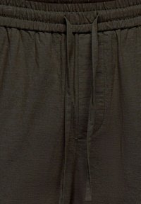 Pantalon à taille élastique marron foncé avec un cordon de serrage au centre avant, fabriqué dans un tissu texturé.