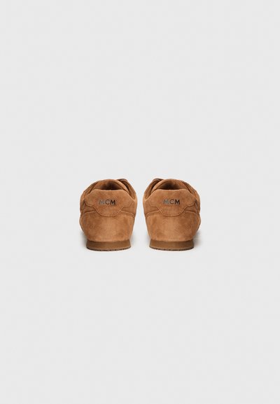 Baskets en daim marron avec une texture lisse, présentant un design basse-tige et un logo MCM sur le talon. Semelles en caoutchouc et forme arrondie.