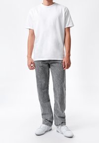 Camiseta blanca de algodón, manga corta; combinada con jeans gris claro de corte relajado con textura desgastada; zapatillas blancas completan el conjunto.