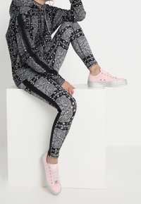 Sudadera con estampado de paisley en blanco y negro y leggins a juego con franjas laterales negras, combinados con zapatillas rosas con cordones y suelas brillantes.