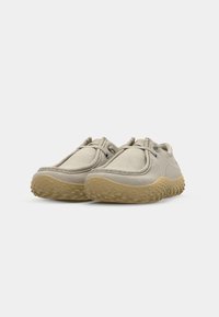 Beige kanva sko med en teksturert gummisåle, rund design og elastiske lisser. Har sømdetaljer og en lav profil.