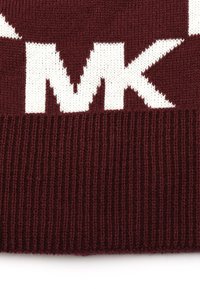 Pull en tricot bordeaux avec des motifs géométriques blancs et un ourlet côtelé. Texture douce avec de grandes lettres intégrées dans le design.
