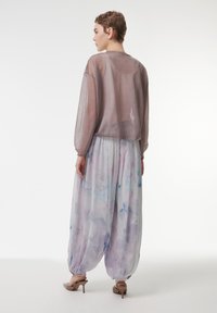 Transparant, metallic bruin cropped sweater met lange mouwen, gelaagd over lichte, luchtige, pastelgekleurde broek met een aquarelpatroon.