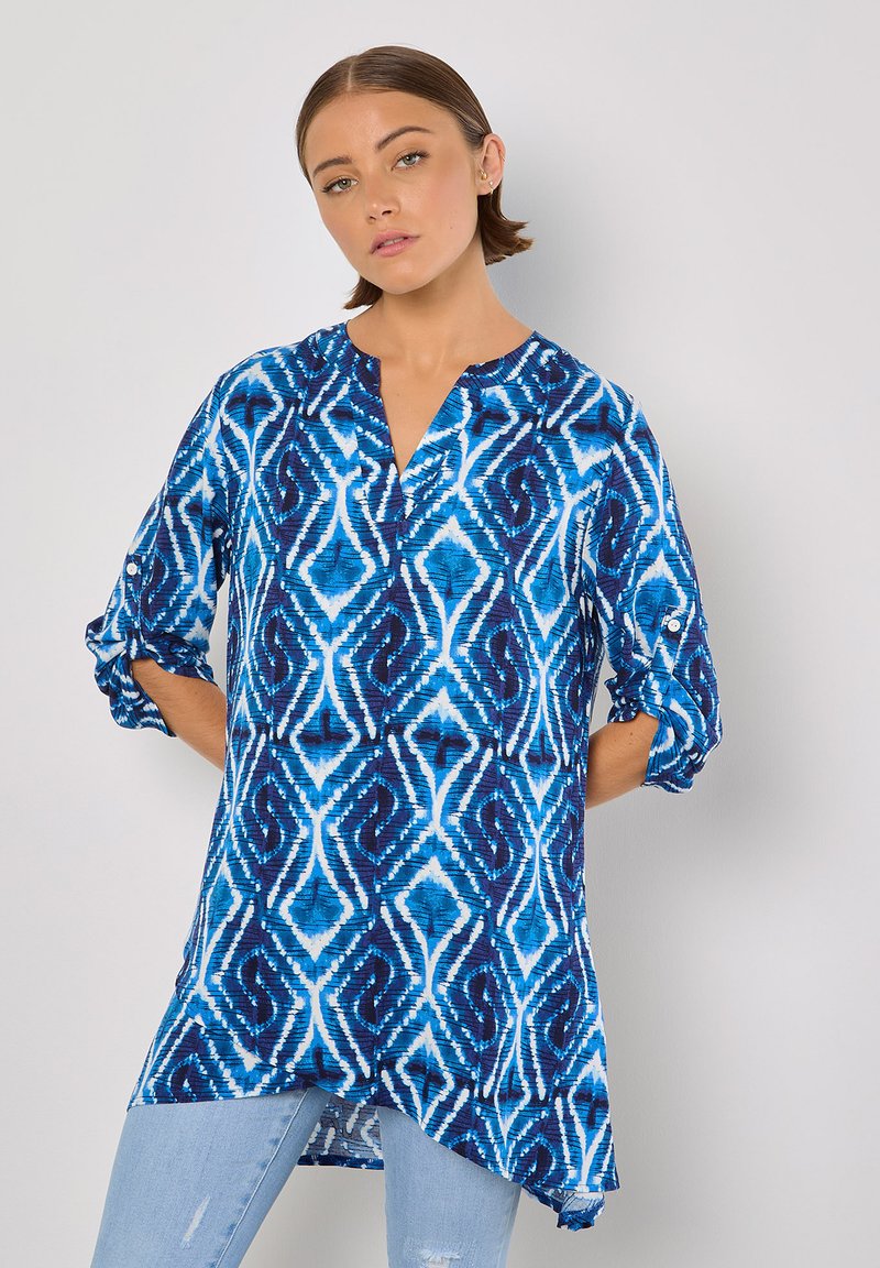 Blaue und weiße Tunika mit geometrischem Muster, V-Ausschnitt und hochrollbaren Ärmeln. Aus leichtem Stoff mit lockerer Passform gefertigt.