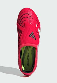 Röd sportskor med texturerad syntetisk ovandel, svarta accentstrimmor och elastiskt band. Insidan har en ljusgrön foder och texten "PREDATOR".