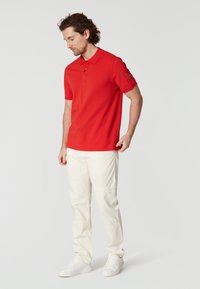 Červené polo tričko, krátké rukávy, s límečkem a zapínáním na knoflíky. V kombinaci se světlými béžovými kalhotami a bílými teniskami. Minimalistický design.