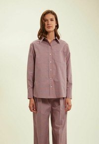 Chemise à carreaux légère rouge, bleue et blanche. Présente un col pointu et des manches longues. Associée à un pantalon à carreaux assorti.