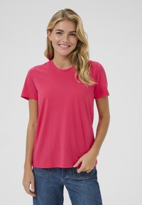 T-shirt à manches courtes, col rond, en coton rose vif, avec une coupe décontractée et une texture douce. Porté avec un jean en denim bleu.