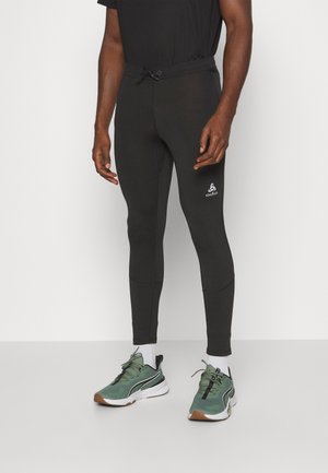 Black athletic leggings featuring a drawstring waist, smooth texture, and a logo accent. Worn with green and black sneakers.