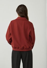 Oversized rode trui met een kraag, zachte textuur, geribbelde manchetten en zoom, gecombineerd met zwarte geruite broek.