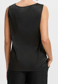 Top senza maniche in satin nero indossato da una persona vista da dietro, abbinato a pantaloni neri con texture e mano in tasca.