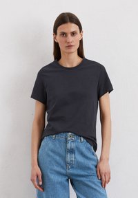 T-shirt in cotone grigio scuro con maniche corte, scollatura rotonda e vestibilità rilassata, abbinato a jeans a vita alta azzurri.