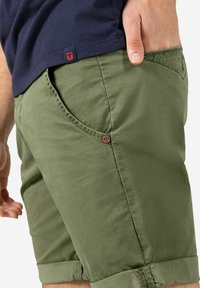 Olivgrüne Shorts aus leichtem Stoff, mit einer vorderen Tasche und runden, braunen Knopfdetails sowie umgeschlagenen Säumen.