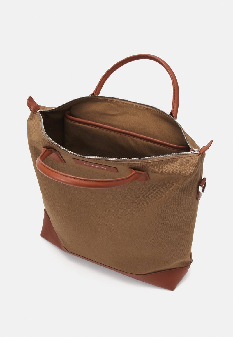 Braune Canvas-Shopper-Tasche mit einem Reißverschluss, Ledergriffen und einer Innentasche. Sie hat eine strukturierte Form und eine glatte Oberfläche.