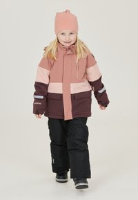 Barnens vinterjacka i rosa och mörkbrun, med en ficka med dragkedja, kontrasterande paneler och reflexdetaljer. Svarta skidbyxor och stövlar.