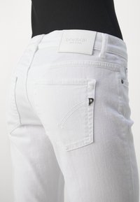 Valkoiset farkut, joissa on vartaloa myötäilevä muotoilu, takataskut, logopatch vyötäröllä ja huomaamattomat ompeluyksityiskohdat.