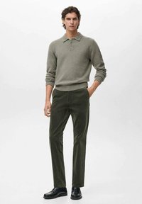 Polo gris de punto con cuello, combinado con pantalones de pana verde oscuro y zapatos negros. Textura suave, diseño ajustado y puños acanalados.