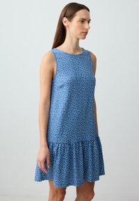 Vestito blu senza maniche con motivo a pois bianchi, scollatura tonda e orlo a volant; realizzato in un tessuto leggero con una texture liscia.