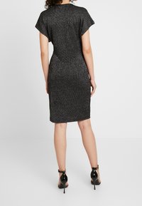 Svart klänning med ribbad textur, korta ärmar och knälång fåll. Stylistiskt kombinerad med svarta högklackade skor och minimala accenter.